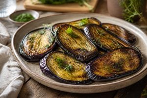 Aubergines à la poêle dorées à l'huile d'olive et à l'ail, servies avec du basilic frais sur une assiette en céramique blanche
