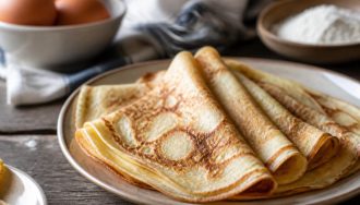 Assiette de crêpes dorées et moelleuses pour 4 personnes, garnies de sucre et de citron, sur une table en bois clair